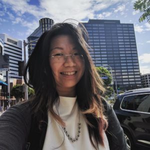 Photograph of Dr. Lynette Lau against a background with high rise buildings and clouds in a blue sky